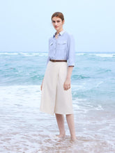 A lady wears a white skirt and a blue shirt.